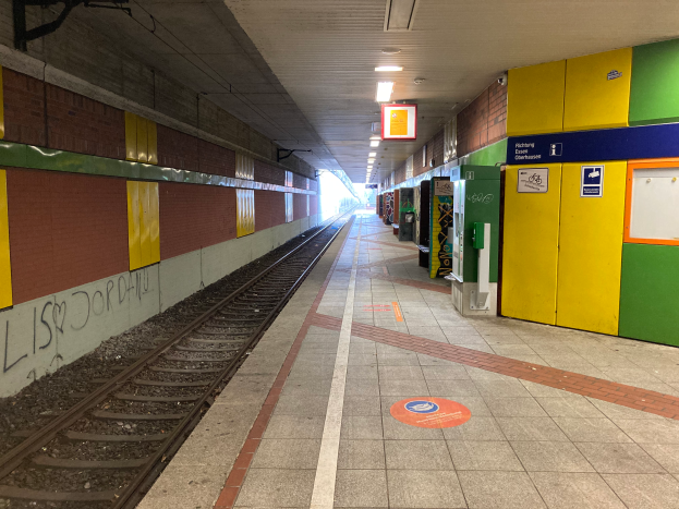 Ein Bahnhof in Berlin, Deutschland, bekannt als Berliner Hauptbahnhof, mit einem Zug auf den Schienen, beleuchtet von Deckenlampen, einer Graffiti-bedeckten Wand auf der linken Seite und ein paar Gegenständen auf der rechten Seite.