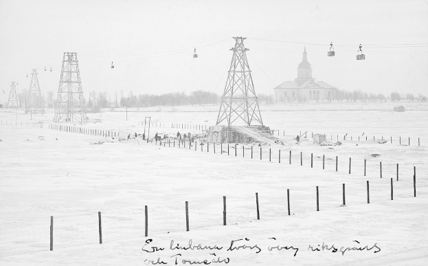 Schwarze-Weiß-Foto eines Skilifts in einer verschneiten Wiese mit Stützpfählen, Überseilbahn, Bäumen und einem Gebäude im Hintergrund, mit Text unten.
