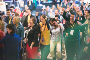 Eine Gruppe von Menschen, die lachend um ein Mikrofon auf einem Ständer stehen.