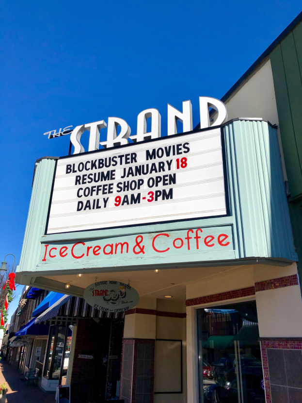 Der Strand-Blockbuster-Kino startet am 18. Januar Kaffeegeschäft mit einem Namensschild, einem Straßenschild, einer Gruppe von Bäumen, einigen Topfpflanzen und einem bewölkten Himmel.