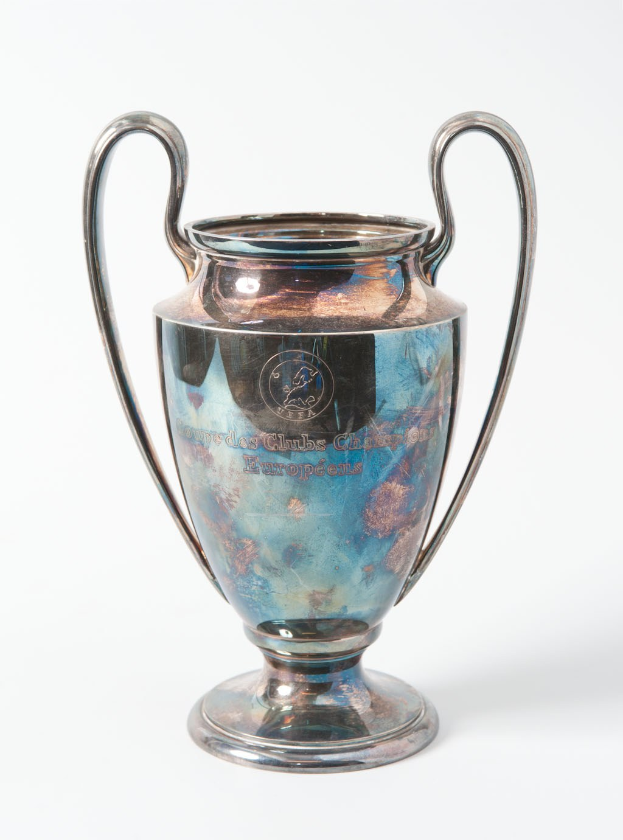 Der UEFA-Champions-League-Pokal, ein stählerner Becher mit zwei Griffen und einem blauen und silbernen Farbschema, der mit 'UEFA Champions League' eingraviert ist, vor einem weißen Hintergrund.