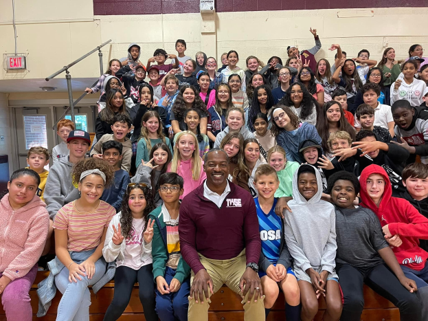 Gruppe von Schülern, die in einem Turnsaal für ein Foto posieren, wobei einige auf der Treppe sitzen und andere stehen, eine Tür und ein Ausgangsschild links sichtbar