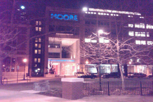 Ein Krankenhausgeb√§ude mit mehreren Fahrzeugen, B√§umen und einem Zaun davor.