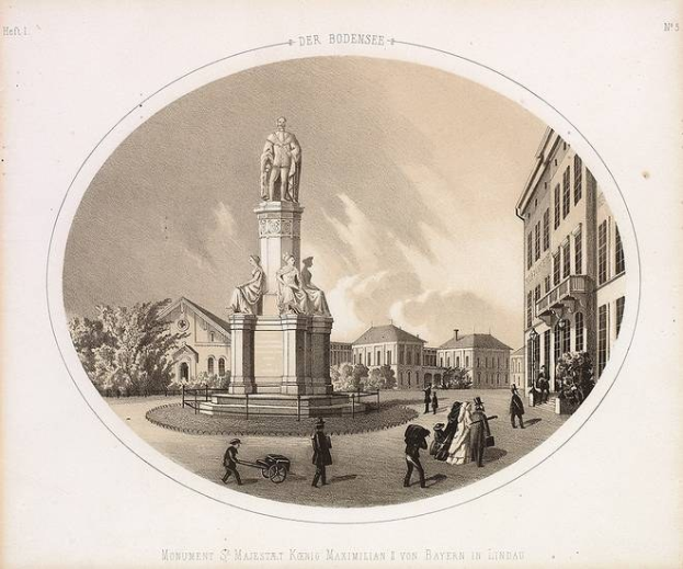 Schwarze und weiße Zeichnung der Statue des Heiligen Majestrat König Maximilian I. von Bayern in einem Stadtplatz, umgeben von Gebäuden, Bäumen und Menschen, mit Text unten.