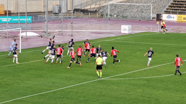 Gruppe von Menschen beim Fußballspielen auf einem Feld mit Zuschauern in einem Stadion.