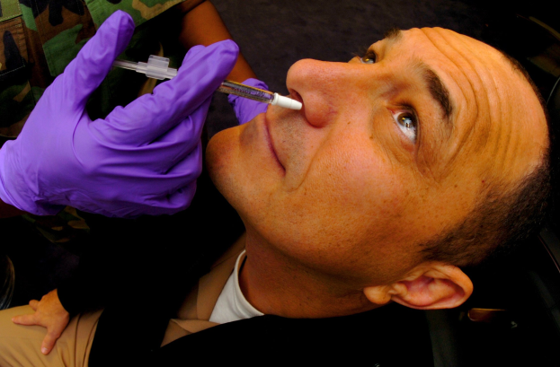 Ein Arzt in lila Handschuhen injiziert einem Mann ein Vakzin mit einer Spritze in den Mund.