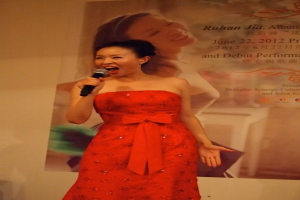 Eine Frau steht mit einem Mikrofon und singt mit einem Plakat im Hintergrund.