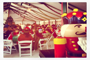 Eine Gruppe von Menschen, die Weihnachten in einer Hütte feiern, mit einem geschmückten Baum, weißen Stühlen, einem roten Spielzeug-Sicherheitsmann und einer schwarzen Krone.