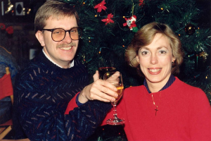 Ein Paar lächelt beim Weintrinken mit einem Weihnachtsbaum im Hintergrund.