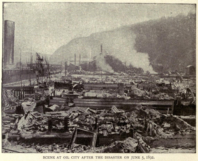 Schwarz-weiß-Foto einer Stadt nach einer Katastrophe am 5. Juni 1892, das Gebäude, Masten, Rauch und einen Hügel im Hintergrund zeigt, mit Text unten.