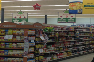 Ein Supermarktinneres mit sichtbaren Lebensmitteln, Deckenlampen und Schildern.