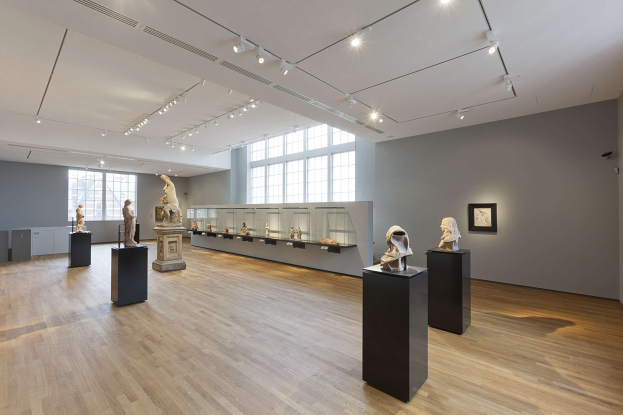 Ein großer Galerieraum mit zahlreichen Statuen auf Sockeln, einem Rahmenbild an der Wand, Glasfenstern und Deckenleuchten in der National Gallery of Victoria in London.