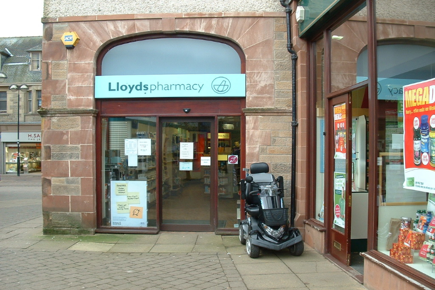 Eine Apotheke mit einem vor ihr geparkten Fahrzeug und einem Gebäude in der linken Ecke.