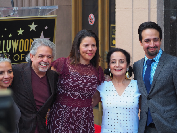 Gruppe von Menschen auf einem roten Teppich bei der Hollywood Walk of Fame Zeremonie, mit einer Kamera links und einer Tafel, einem Podium und einer Wand im Hintergrund.