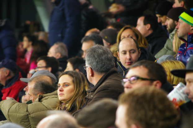 Eine Menschenmenge auf Tribünen eines Stadions, die ein Fußballspiel angucken, mit einem Mann und einer Frau im Vordergrund.
