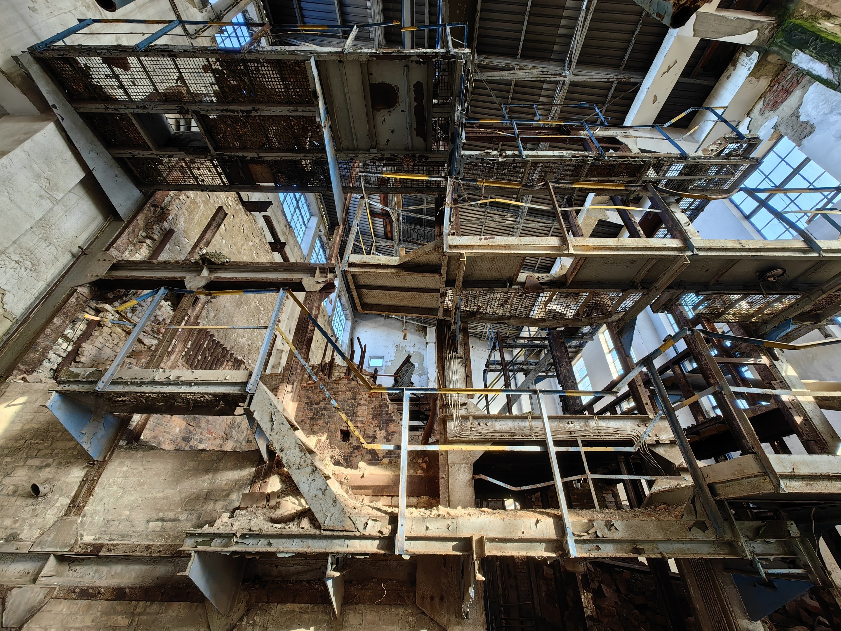 Altes industrielles Gebäude mit einer zentralen Metallstruktur, umgeben von verrosteten Eisenstäben, Treppen, Wänden und Fenstern, zeigt Zeichen von Verfall und Verfall.