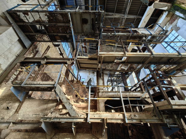 Altes industrielles Gebäude mit einer zentralen Metallstruktur, umgeben von verrosteten Eisenstäben, Treppen, Wänden und Fenstern, zeigt Zeichen von Verfall und Verfall.