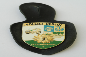 Ein Polizeistern aus Berlin, der wie ein Schild geformt ist, mit einem blauen Hintergrund, einem weißen Stern in der Mitte und einem weißen Rand, mit den Worten "Polizei Berlin" in fetter schwarzer Schrift.