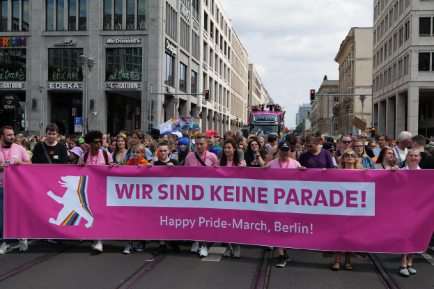 Eine Gruppe von Menschen geht auf einer Straße in Berlin, Deutschland, mit einer pinken Fahne mit der Aufschrift "Happy Pride March"