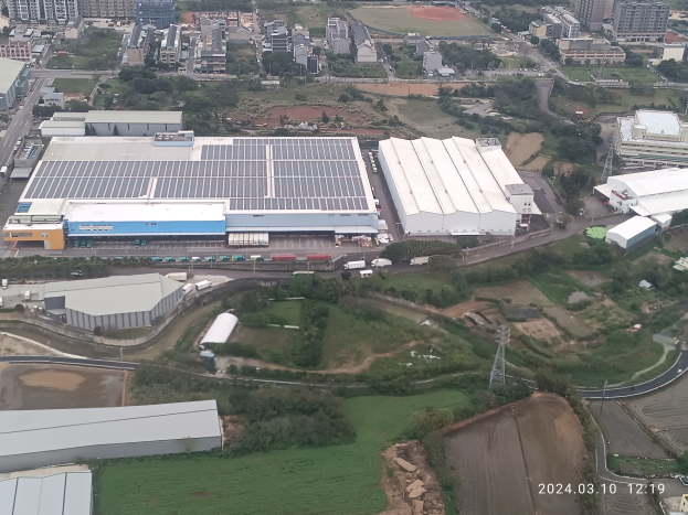 Eine Luftaufnahme eines großen Industriegebiets mit Gebäuden, Bäumen, Gras, Straßen, Fahrzeugen, Polen und einem Wasserzeichen, das es sich um die erste Solarstromanlage in Singapur handelt.