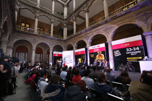 Eine Gruppe von Menschen, die an einem Tisch mit einem Podium und einem Mikrofon vor einer Menge, Kameras und Transparenten sitzen, während einer Pressekonferenz für das CDMX 2017-Event.