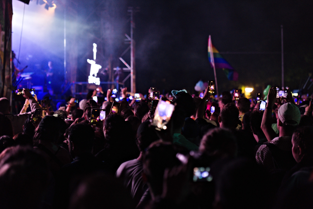 Menge von Menschen auf einem Konzert mit leuchtenden Handys in der Luft, während Musiker auf der Bühne spielen