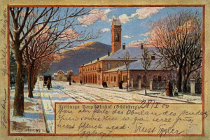 Eine alte Postkarte zeigt ein schneebedecktes Gebäude umgeben von Bäumen, Menschen und einem Zaun, mit der Aufschrift "Freiburg Hauptbahnhof" unten.