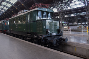 Ein Zug auf Schienen mit Geländern und Planken im Hintergrund, Lampen auf dem Dach und ein Himmel darüber, mit einem Boden darunter.