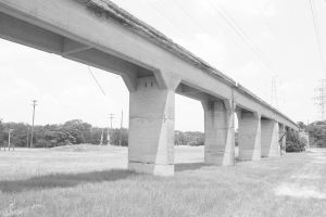 Eine Betonbrücke auf einem grünen Rasen mit einem großen elektrischen Mast und Kabeln darüber, umgeben von Bäumen und zusätzlichen elektrischen Masten im Hintergrund.