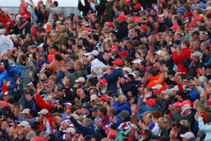 Eine große Menge von Menschen, viele mit roten Mützen, versammelte sich vor einem Zaun.