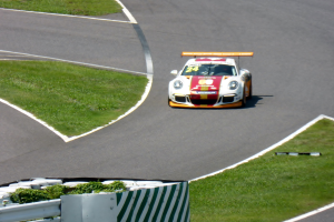 Ein Porsche 911 GT3 RSR auf der Nürburgring 24-Stunden-Rennstrecke, umgeben von grünem Gras und einem Geländer, wobei die bunten Farben und die elegante Form des Autos deutlich sichtbar sind.