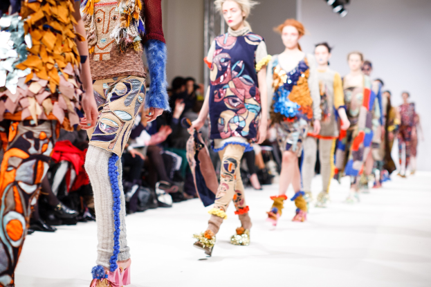 Eine Gruppe Von Frauen, Die Eine Laufsteg In London Fashion Week Heruntergehen, Mit Einem Publikum Im Hintergrund Unter Helleren Lichtern, Schaffend Ein Etwas Verwischtes, Traumhaftes Effekt.