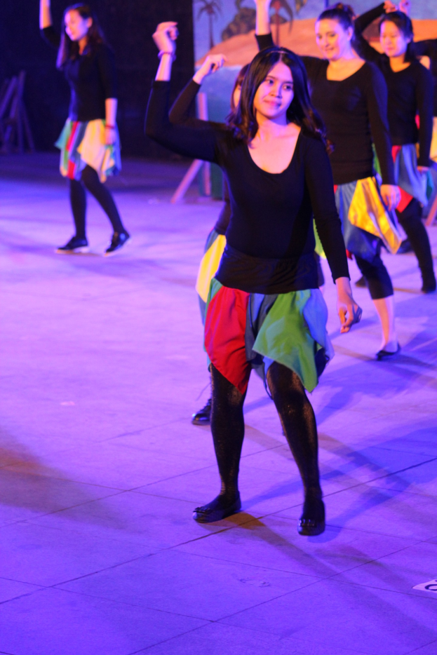 Junge Frauen tanzen auf einer Bühne mit einem Gemälde an der Wand im Hintergrund, tragen Schuhe während einer Vorstellung.