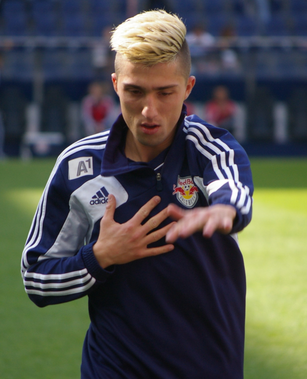 A young man in a blue Everton FC jersey stands on a soccer field in a stadium.