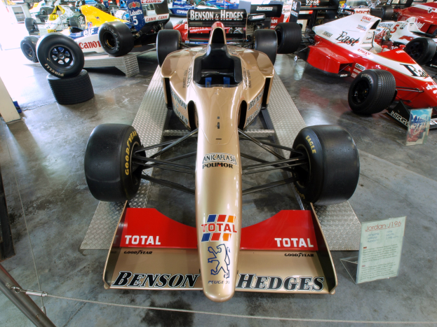 Rennwagen in einem Motorsportmuseum ausgestellt, getrennt von Besuchern durch einen Metallzaun.