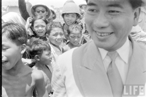 Ein Schwarz-Weiß-Bild von Kindern mit einer Person auf der rechten Seite, die Kleidung trägt und einen Text in der rechten unteren Ecke.