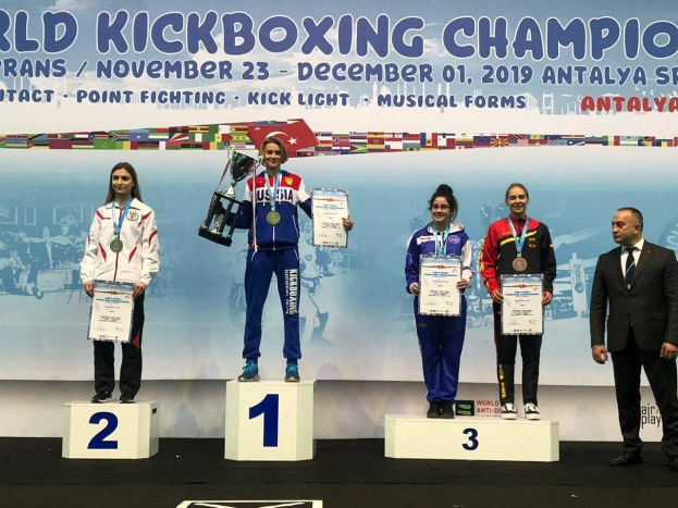 Fünf Personen auf einem Podium mit Trophäen und Urkunden in den Händen, im Hintergrund ein Banner mit der Aufschrift "World Kickboxing Championship Antalya 2019".
