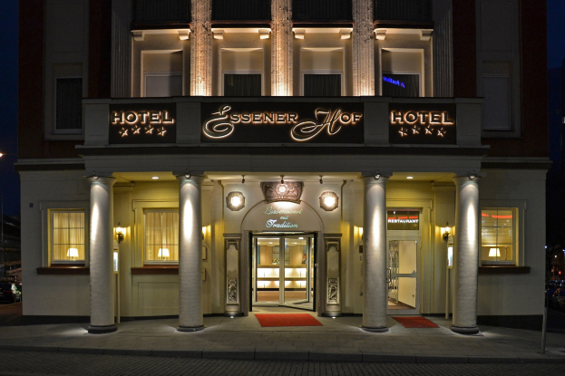 Das Essenerhof Hotel in Berlin, Deutschland, ein mehrstöckiges Gebäude mit Fenstern, Türen, Säulen, Laternen und einem Namensschild, mit einer Straße davor und Fahrzeugen auf der rechten Seite, unter einem sichtbaren Himmel.