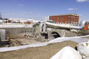 Eine Szene mit Gebäuden, einem Zaun, Fahrzeugen, aktuellen Umfragen, einem Rohr und dem Himmel darüber.
