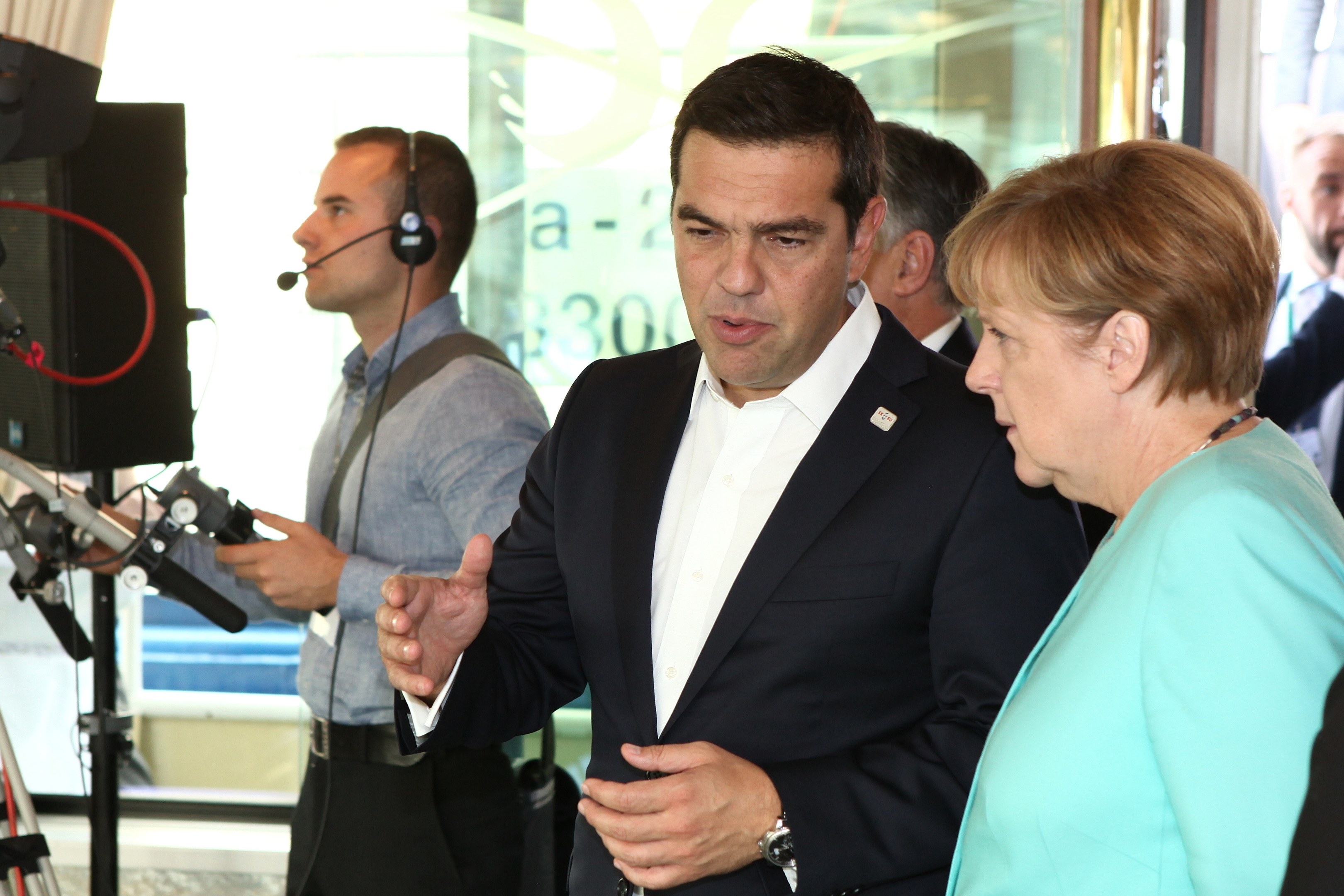 Zwei deutsche Bundeskanzler, Angela Merkel und Joachim Gauck, stehen vor einer Glaswand mit einem Vorhang dahinter, beide tragen Anzüge und Mikrofone.