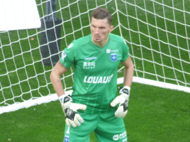 Ein Torwart in grünem Trikot steht auf grünem Rasen vor einem Fussballtor und trägt Handschuhe.