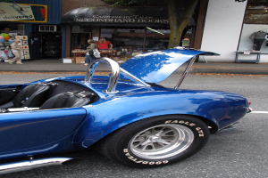 Ein blaues Fahrzeug auf der Straße mit Geschäften und Menschen im Hintergrund.