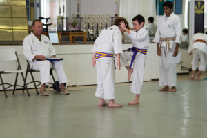 Zwei Kinder beim Kung-Fu-Training mit ihrem Meister, der links am Tisch sitzt und etwas prüft.