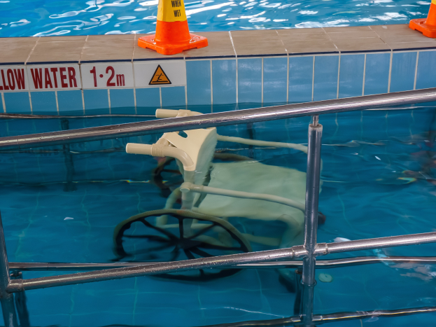 Ein Schwimmbad mit einem Stuhl in der Mitte, umgeben von Sicherheitskegeln und einem Geländer und einem Schild an der Wand, das verfügbare Schwimmausrüstung anzeigt.