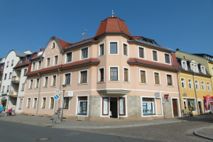 Ein großes Rathaustor mit einem Uhrenturm, umgeben von Straßenlaternen, Schildern, Fahrzeugen, Passanten und einem bewölkten Himmel.