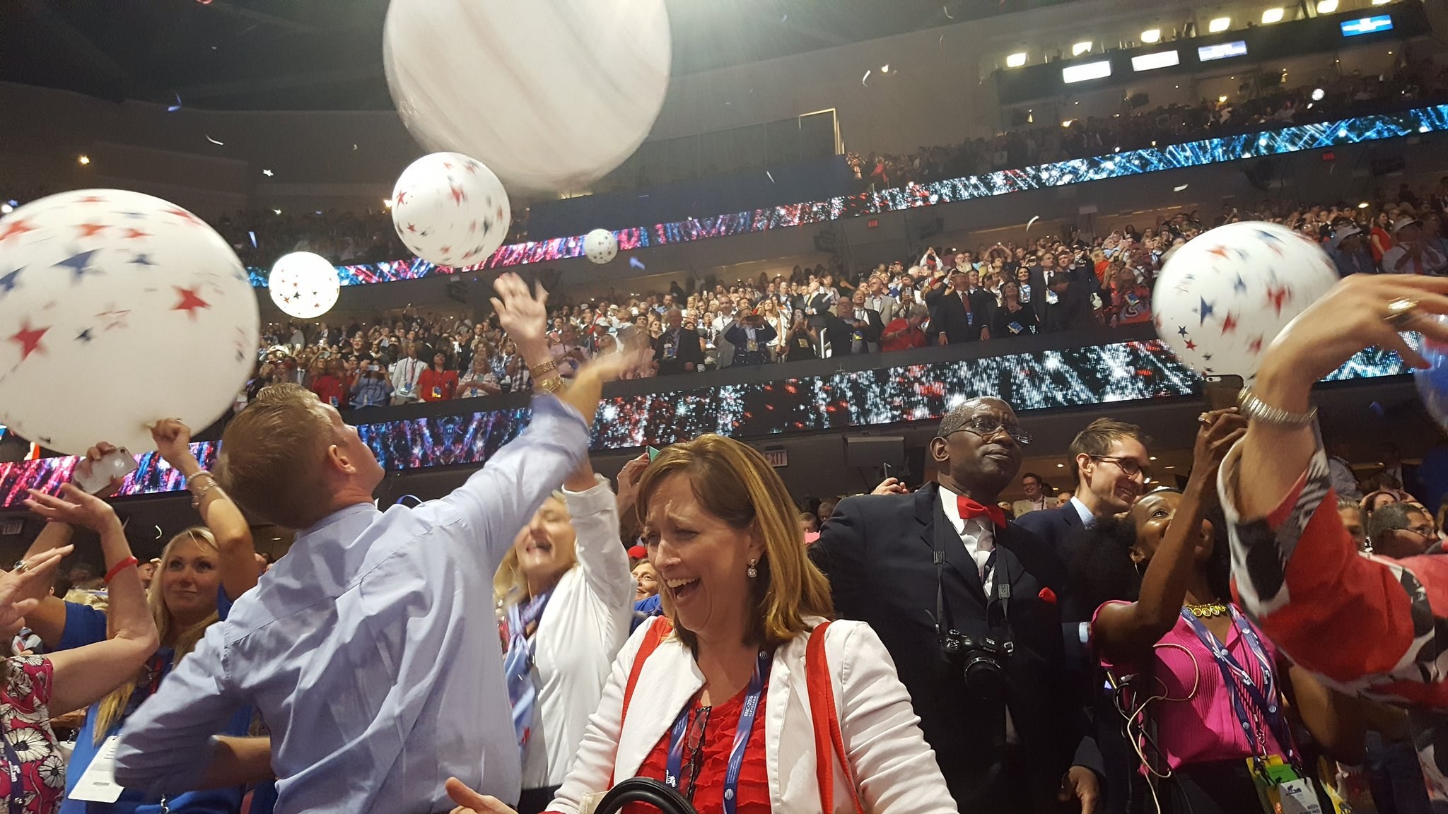 Eine Menschenmenge mit Luftballons steht vor sitzenden Zuschauern bei einem beleuchteten Ereignis, das wahrscheinlich den Sieg bei einer Republican National Convention feiert.
