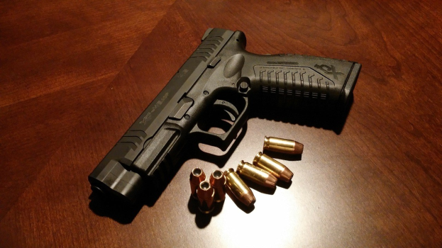 Schwarze Sig Sauer P320 X-Five Pistole mit einem 9mm Magazin auf einem Holztisch, begleitet von Patronen in verschiedenen Größen und Farben.