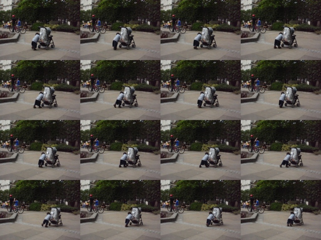 Ein Kind läuft auf einer Straße und zieht einen Einkaufswagen, während zwei Personen Fahrräder halten, Bäume im Hintergrund und ein Gebäude auf der linken Seite.