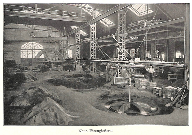 Schwarzes und weißes Foto einer Fabrik mit Arbeitern, die Maschinen bedienen, Metallstangen und -pfähle, beschriftet mit "Neue Eisengießerei, die erste Fabrik in Deutschland" unten.
