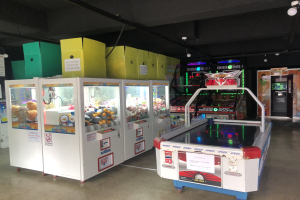 Ein Raum voller verschiedener Arcade-Spiele, mit einem Spielautomaten auf der rechten Seite, einem sichtbaren Boden und Deckenbeleuchtung.